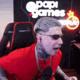 a man wearing sunglasses and a red shirt is sitting in front of a papa games sign