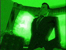 a man in a suit and tie is standing in front of a window with a green light behind him .