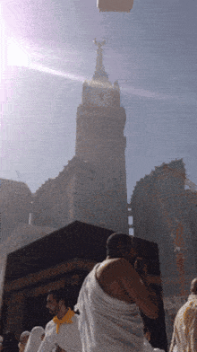 a man in a white robe stands in front of a large building with a clock tower in the background