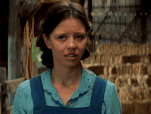 a woman in a blue shirt and blue overalls is making a face