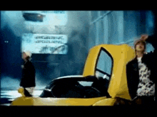 a man is standing next to a yellow sports car with its hood open .
