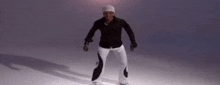a man wearing a black shirt and white pants is dancing on a white surface .
