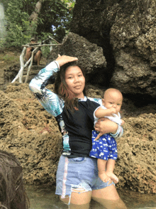 a woman holding a baby in the water wearing a rash guard