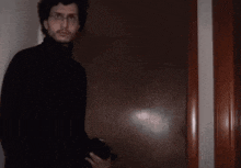 a man in a black turtleneck and glasses is holding a camera