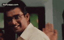 a man wearing glasses and a white shirt is waving his hand .