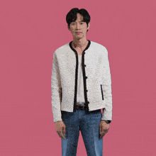 a man wearing a white sweater and blue jeans is standing in front of a pink background