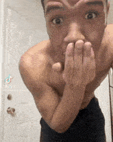 a man without a shirt is covering his mouth with his hand .