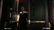 a man in a suit and tie walks through a doorway with a nbc logo in the corner