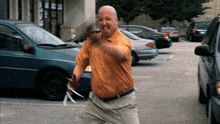 a bald man in an orange shirt is holding a pair of scissors