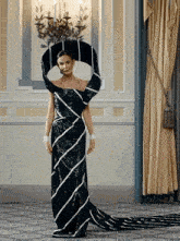 a woman in a black and white striped dress stands in front of a chandelier