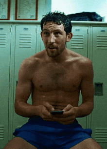 a shirtless man is sitting in front of lockers with the letters uc on them