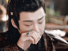 a close up of a man with a ring on his finger covering his mouth .