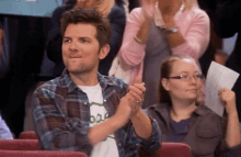 a man in a plaid shirt is applauding in a crowd .
