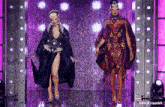 two drag queens are dancing on a stage with a purple curtain in the background