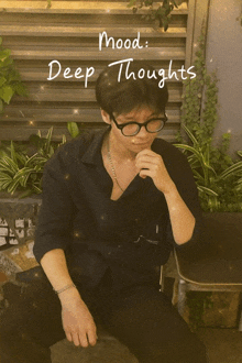 a man wearing glasses is sitting in front of a sign that says mood deep thoughts
