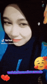 a woman wearing a hijab and a blue shirt has a tiktok sticker on her face