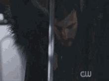 a man is standing in front of a wall with a cw logo on the bottom right
