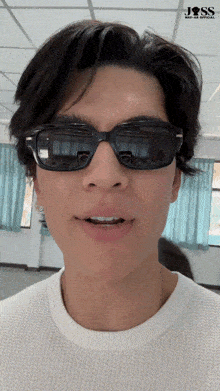 a man wearing sunglasses and a white sweater has a jss logo on the ceiling