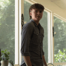 a man in a grey shirt stands in front of a large window