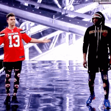 a man in a red jersey with the number 13 on it stands next to another man