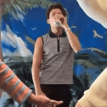 a man in a striped shirt is drinking from a can while standing in front of a blue background .