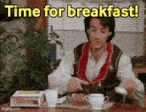 a man is sitting at a table with a tray of food and the words time for breakfast