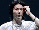 a young man with long black hair is wearing a white t-shirt and a chain around his neck .