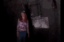 a woman in a purple shirt is standing in a dark room .