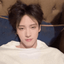 a young man is laying on a couch with his head wrapped in a white blanket and looking at the camera .
