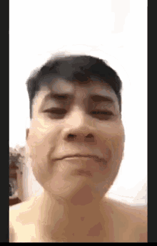 a man without a shirt is making a funny face in front of a white wall .