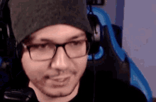 a man wearing glasses and a beanie is sitting in a chair with headphones on .