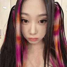 a close up of a woman 's face with pink and orange hair extensions