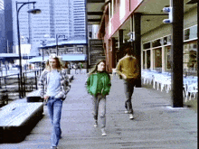 a woman in a green jacket walks down a sidewalk next to a man in a plaid shirt