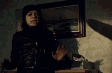 a woman in a black jacket stands in front of a painting on the wall