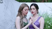 two women are standing next to each other and one is wearing a purple dress and the other is wearing a green dress .