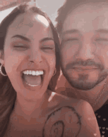 a man and a woman are laughing together and the woman has a tattoo on her arm