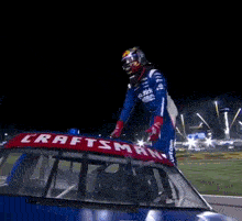 a man stands on top of a craftsman race car with his arms outstretched