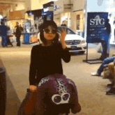 a woman wearing sunglasses is standing in front of a stg sign