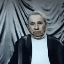 a man in a black jacket and white shirt is making a funny face