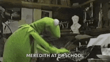 kermit the frog is typing on a typewriter in a room with a statue in the background .