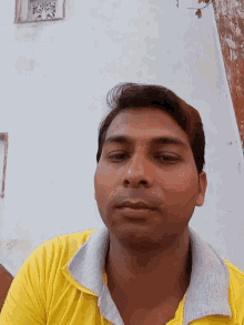 a man wearing a yellow shirt with a white collar looks at the camera