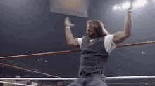 a man is standing in a wrestling ring with his hands in the air .