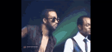 a man wearing sunglasses is standing next to another man in a white shirt and tie .