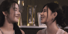 two women are looking at each other and smiling in front of a hourglass