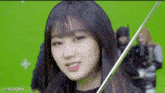 a girl is holding a sword in front of a green screen and sticking her tongue out .