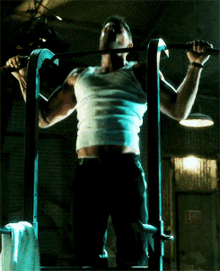 a man in a white tank top is doing a pull up on a bar