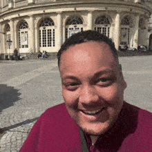 a man in a red shirt is smiling in front of a large building