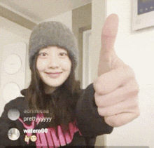 a woman wearing a beanie and giving a thumbs up sign