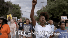 a woman in a white shirt holds her fist in the air with the words free ann now behind her