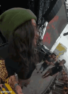 a person wearing a green beanie is standing in front of a crowd at a music festival